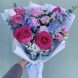 Bouquet of pink and blue roses with white filler flowers wrapped in white paper