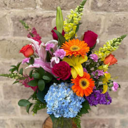 Colorful mixed bouquet in a glass vase with roses, lilies, gerbera daisies, and hydrangea
