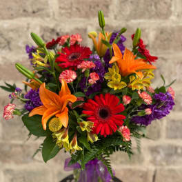 Colorful bouquet with orange lilies, red gerbera daisies, and purple flowers in a vase