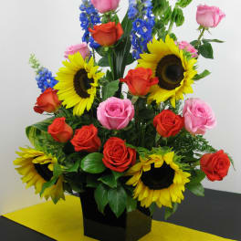 Sunflowers, roses, and blue delphinium in a black vase