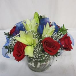 Red roses and pale lilies in a glass vase with blue ribbon