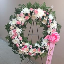 Pink and white floral wreath on a stand with a pink ribbon