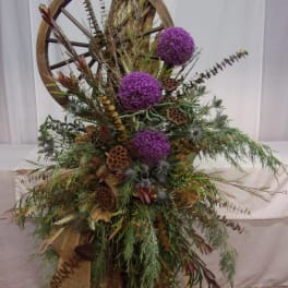 Tall rustic arrangement with purple globe flowers and dried botanicals on a wagon wheel frame