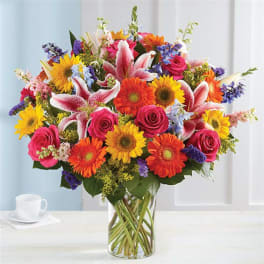Mixed bouquet of sunflowers, roses, lilies, and gerbera daisies in a glass vase