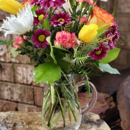 Mixed bouquet of daisies, tulips, and carnations in a clear glass pitcher