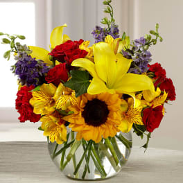 Bright mixed bouquet in a clear glass vase with red, yellow, and purple flowers