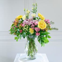 Mixed bouquet of yellow and pink flowers in a clear glass vase on a white surface