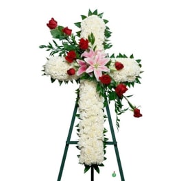 Standing white floral cross with pink lilies and red roses on a green easel