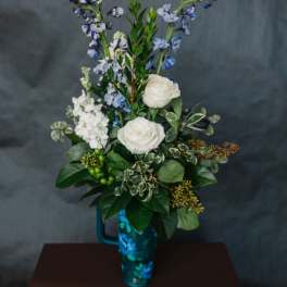 White roses and blue flowers arranged in a tall blue vase