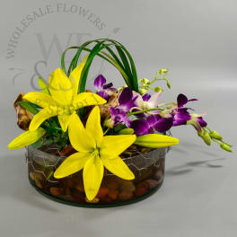 Yellow lilies and purple orchids in a glass bowl with stones