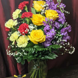 Bouquet of yellow roses, purple stock, and red and pale yellow carnations in a glass vase