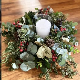 Candle in a glass holder surrounded by a holiday greenery wreath