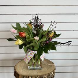 Mixed tulips and greenery in a clear glass vase with a polka-dot ribbon