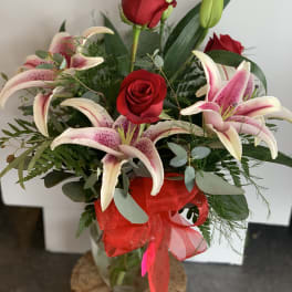 Arrangement of red roses and pink lilies in a clear glass vase with a red bow.