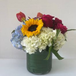 Mixed bouquet in a green glass vase with roses, hydrangeas, and a sunflower