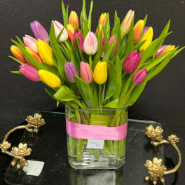Colorful tulips arranged in a clear glass vase with a pink ribbon