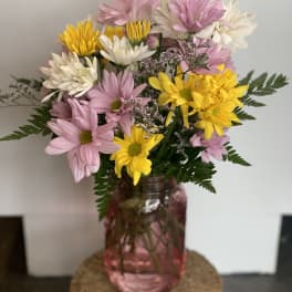 Pink, white, and yellow daisy bouquet in a pink glass vase