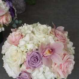 Round bouquet of pink, white, and lavender flowers in a low container