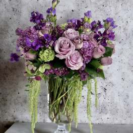 Lavender roses and purple flowers arranged in a clear glass vase
