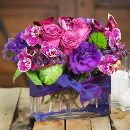Pink roses and purple orchids in a glass vase with a ribbon