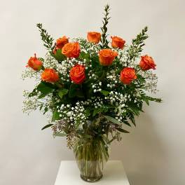 Orange roses arranged in a clear glass vase with white baby's breath