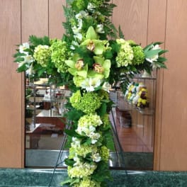 Tall green floral cross with white blooms on a stand