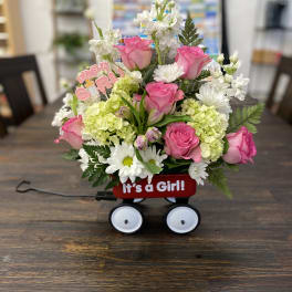 Pink roses and white flowers in a red wagon with an "It's a Girl!" sign