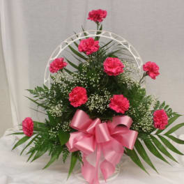 Pink carnation arrangement with a large pink bow in a white basket