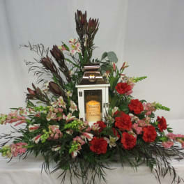 Floral arrangement around a white memorial lantern with red and pink flowers.
