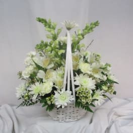 White floral arrangement in a white wicker basket with ribbon handles