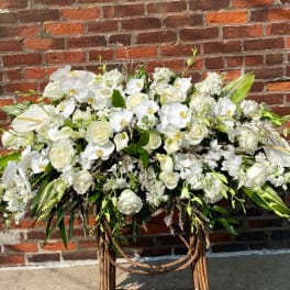 Large white floral arrangement on a stand against a brick wall