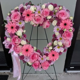 Heart-shaped floral wreath with pink roses and daisies on a stand