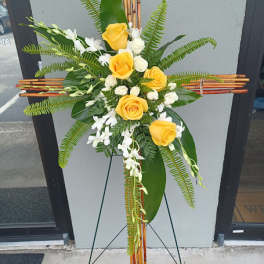 Yellow roses and white flowers arranged on a standing cross