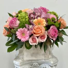 Low arrangement of pink and peach roses, gerbera daisies, orchids and mums in a rustic box vase