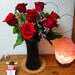 Red roses arranged in a black vase with small pink filler flowers