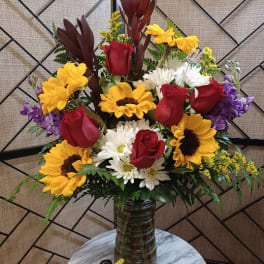 Mixed bouquet of red roses, sunflowers, and white daisies in a glass vase