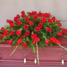 Red rose casket spray with greenery on a burgundy casket