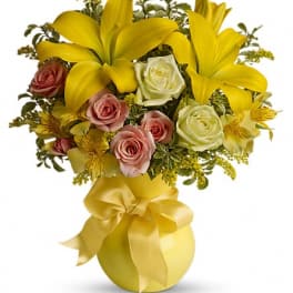Yellow lilies and pink roses arranged in a gold vase with a ribbon bow