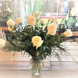 Cream roses arranged in a clear glass vase with airy greenery.