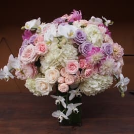 Large pastel bouquet of roses, hydrangeas, and orchids in a dark vase