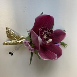 Magenta orchid corsage with small pink blooms and gold glitter accents on a white background