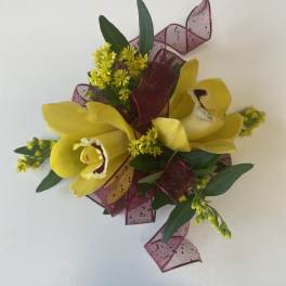 Yellow orchid corsage with burgundy ribbon and greenery