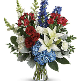 Mixed bouquet of red roses, white lilies, blue flowers, and hydrangeas in a glass vase