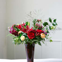 Red roses and lilies arranged in a tall burgundy vase