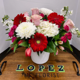 Bouquet of red gerbera daisies, pink roses, and white blooms in a white vase