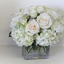 White roses and hydrangeas arranged in a clear square vase