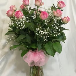 Pink roses with baby's breath in a clear glass vase tied with a pink bow