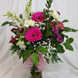 Mixed bouquet with pink gerbera daisies, white snapdragons, and purple blooms in a glass vase