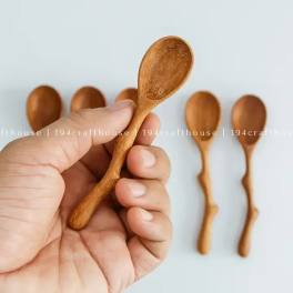 Hand holding a small wooden spoon with more spoons in the background
