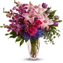 Pink lilies, roses, orchids, and blue hydrangeas in a clear vase